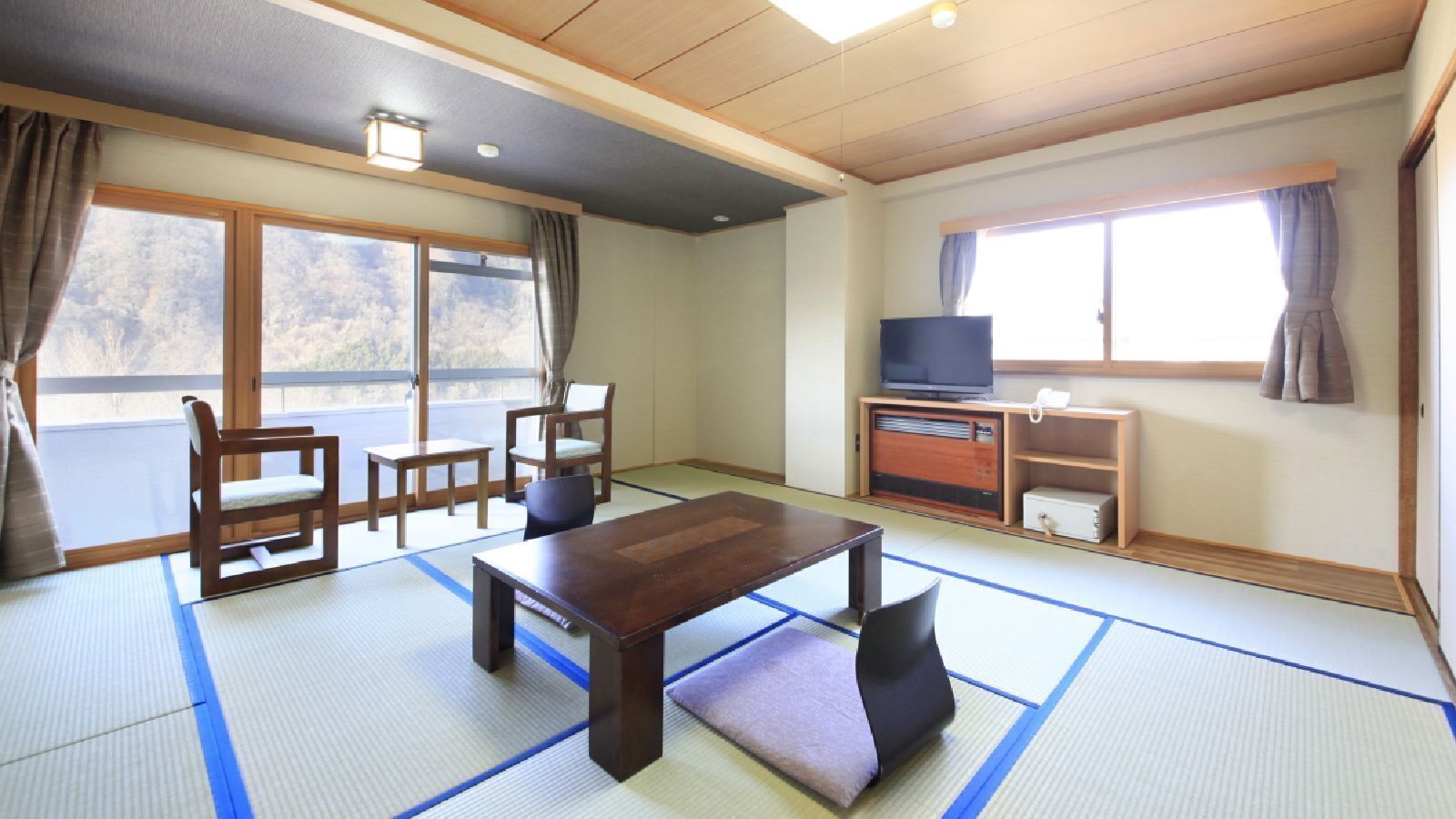 Una habitació japonesa tradicional amb paviment de tatami, una taula baixa, cadires, televisió i una porta corredissa que dona a un balcó.