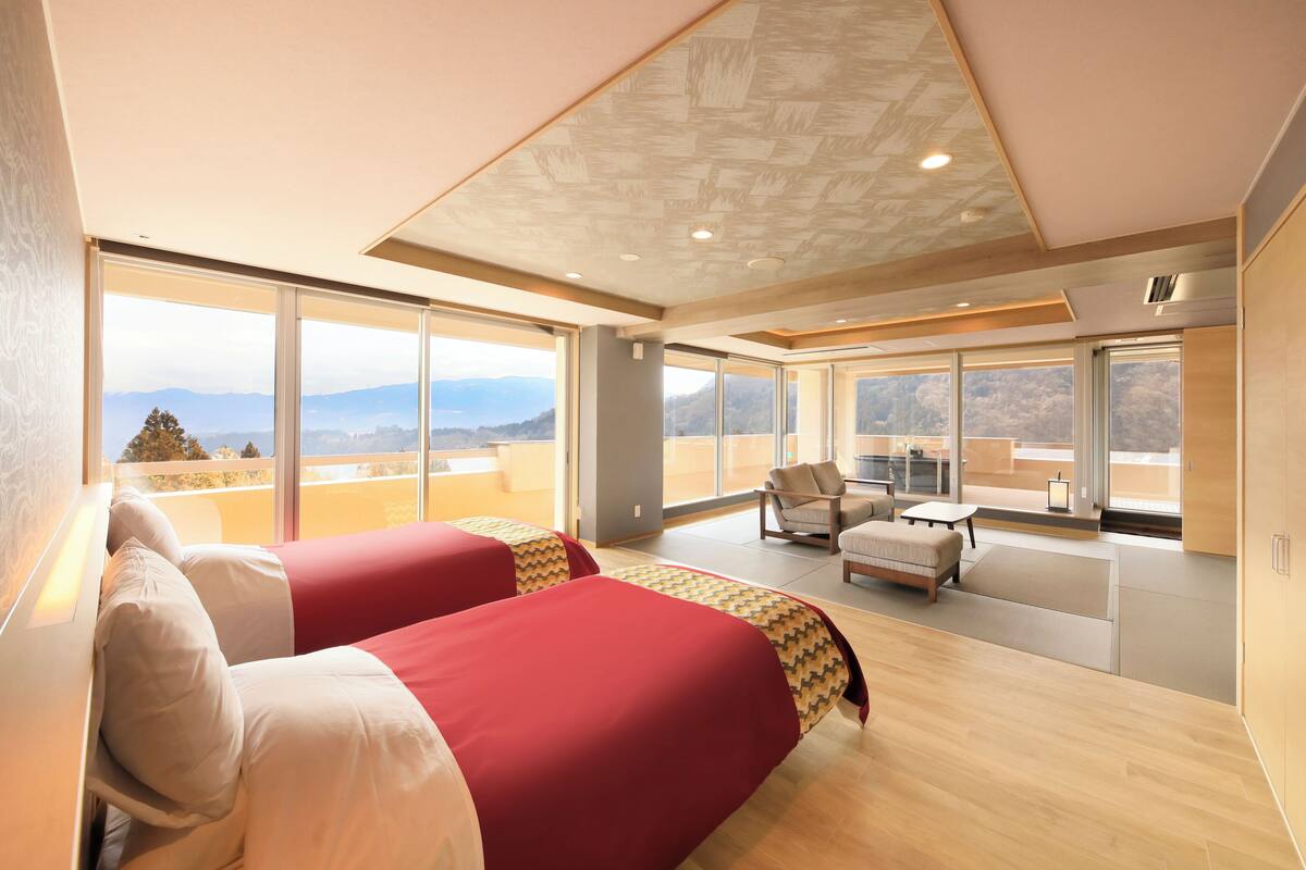 A modern hotel room with large windows, a balcony, and a view of the mountains.