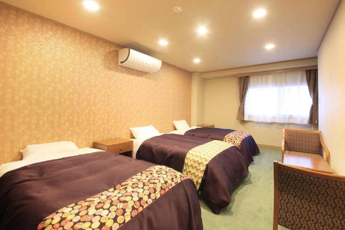 A hotel room with three beds, a desk, and a chair.