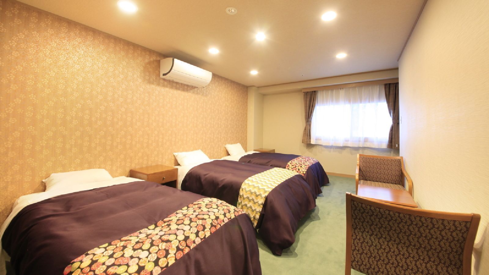Habitació d'hotel amb tres llits, un escriptori i una cadira.