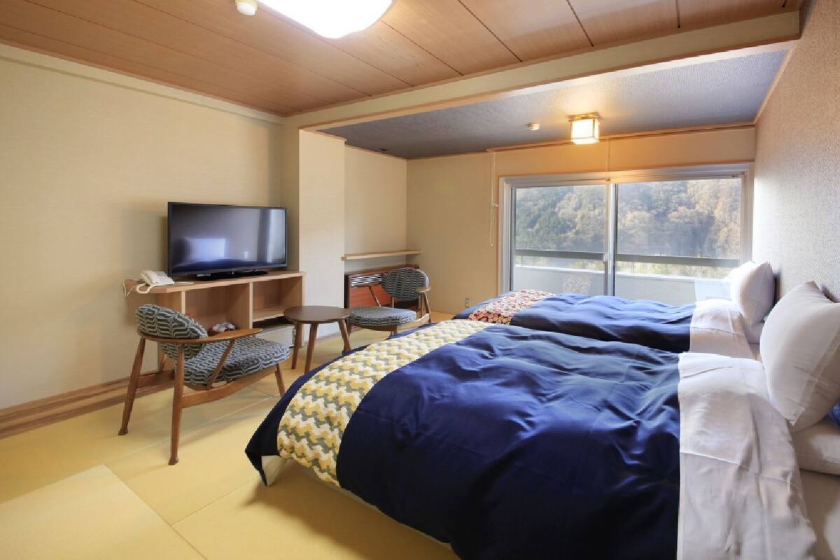 A bedroom with a bed, a television, a desk, and a window.