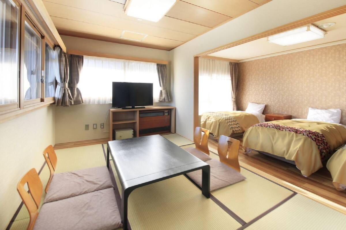 A room with two beds, a television, a table, and chairs.