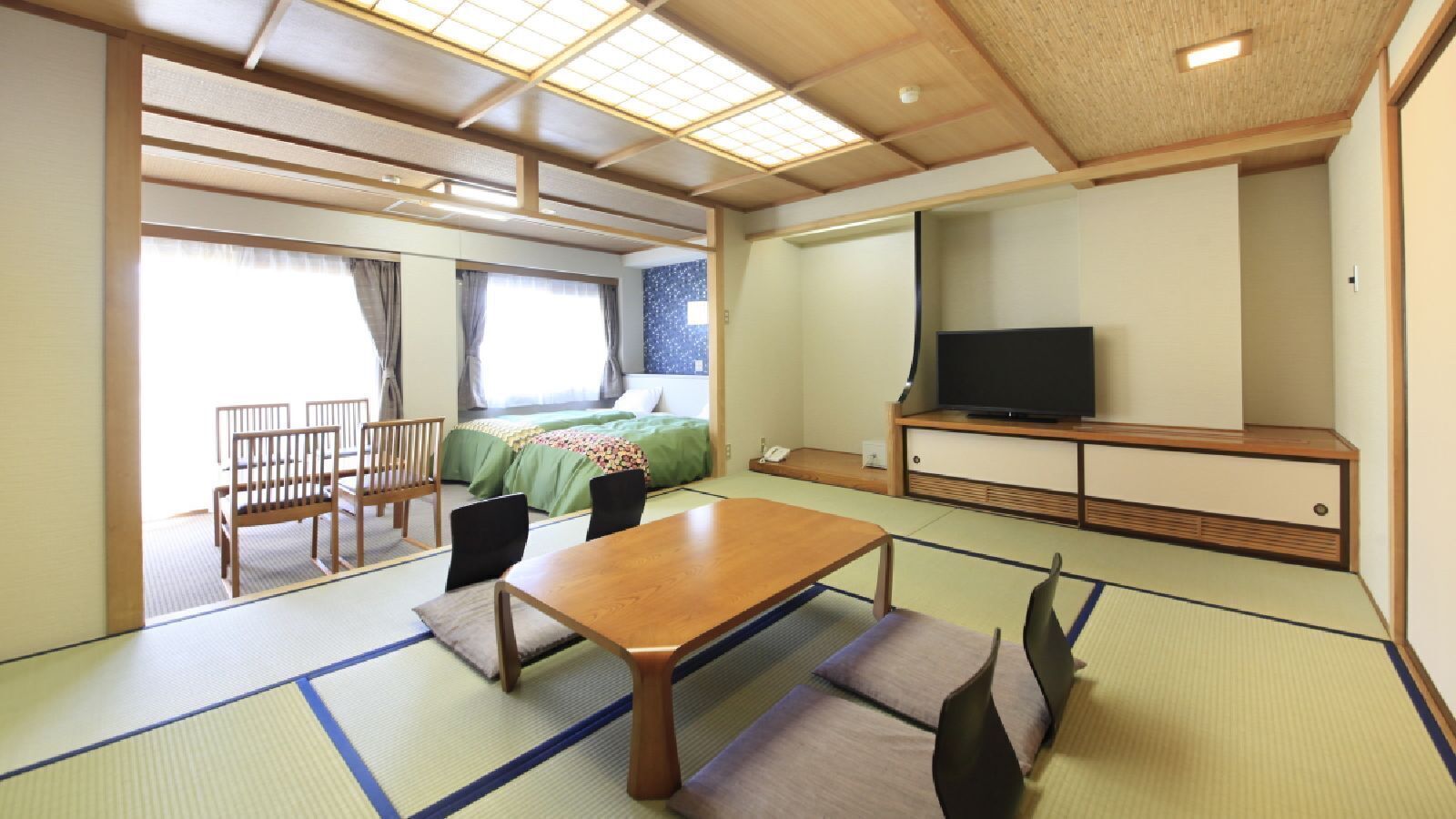 Habitació tradicional japonesa amb fusta de tatami, una taula baixa, cadires, un llit i una televisió.