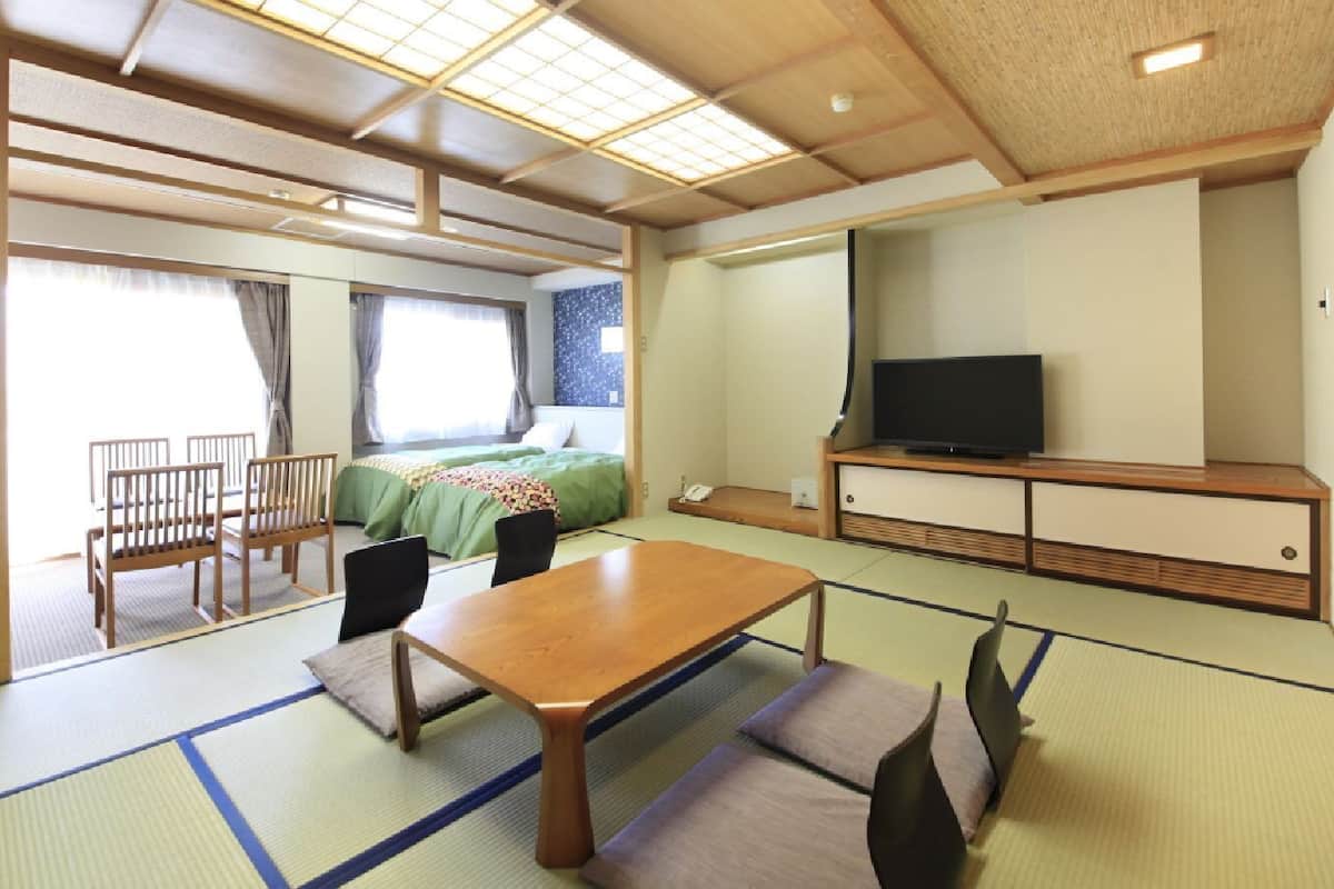 Habitació tradicional japonesa amb fusta de tatami, una taula baixa, cadires, un llit i una televisió.
