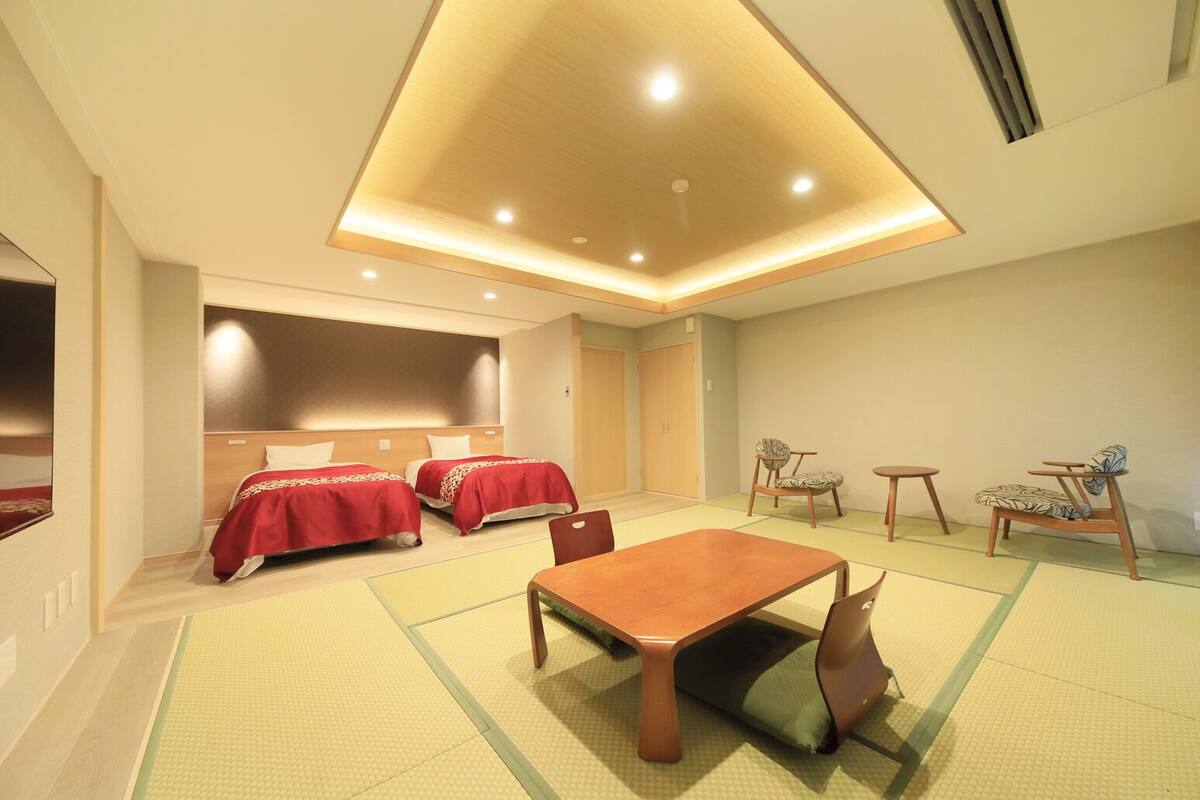 A hotel room with two beds, a dining table, chairs, and a small seating area.