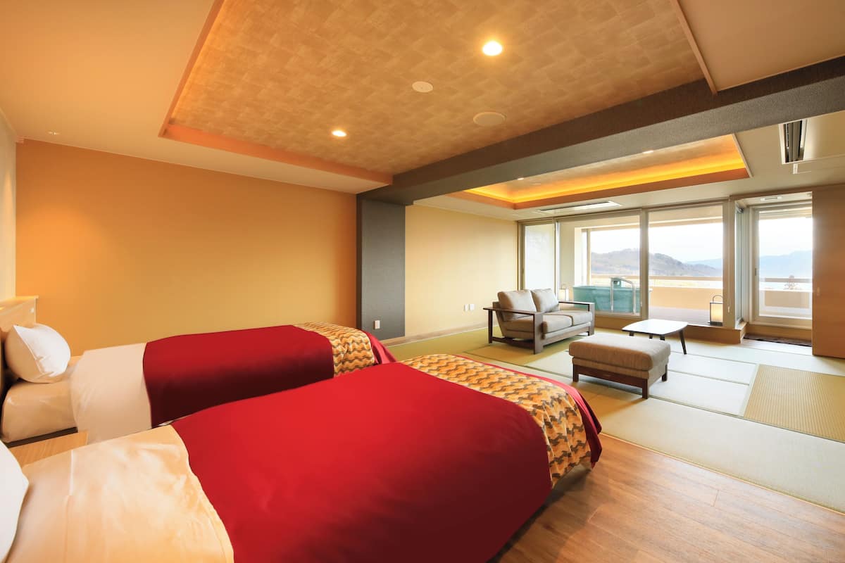 A hotel room with two beds, a sofa, a small table, and a view of the mountains.