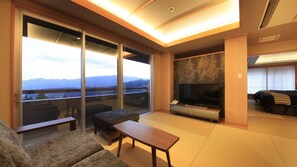 Un salon moderne doté d’un grand téléviseur, d’un canapé, d’une table basse et d’une porte-fenêtre coulissante donnant sur un balcon avec vue sur les montagnes.