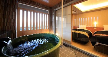 Habitación con una bañera grande, dos camas con ropa oscura y vistas a una estructura de madera en el exterior.