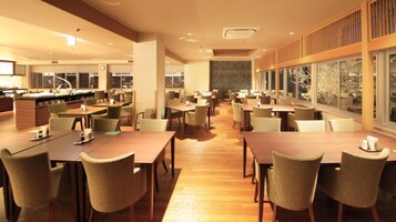 Un comedor amplio con varias mesas y sillas, una cocina al fondo y ventanas grandes que ofrecen vistas.