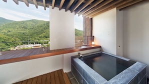 Un área de spa con jacuzzi, terraza de madera y vistas a un paisaje verde.