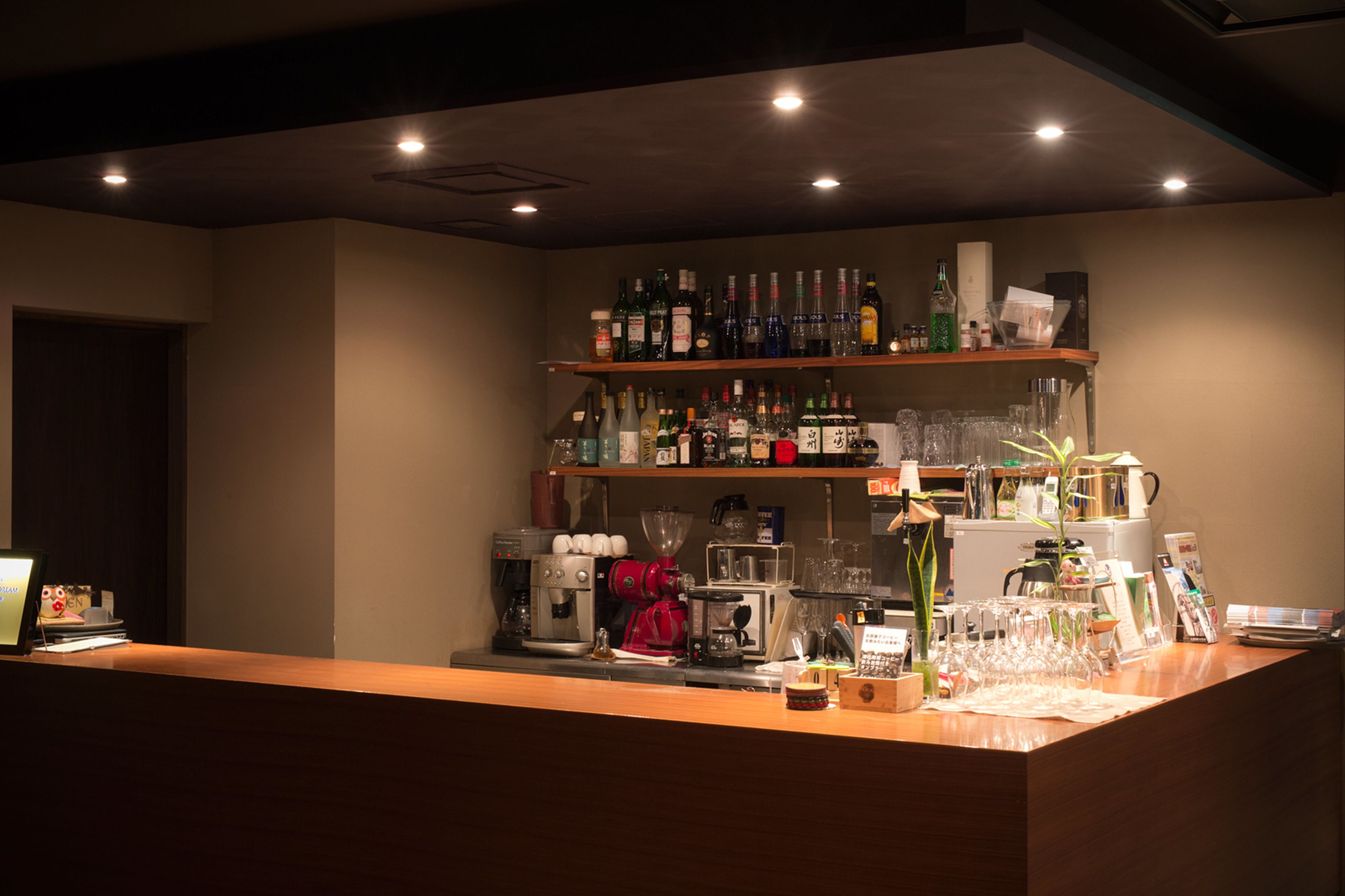 A bar area with shelves of bottles, a coffee machine, and a counter with glasses and a plant.