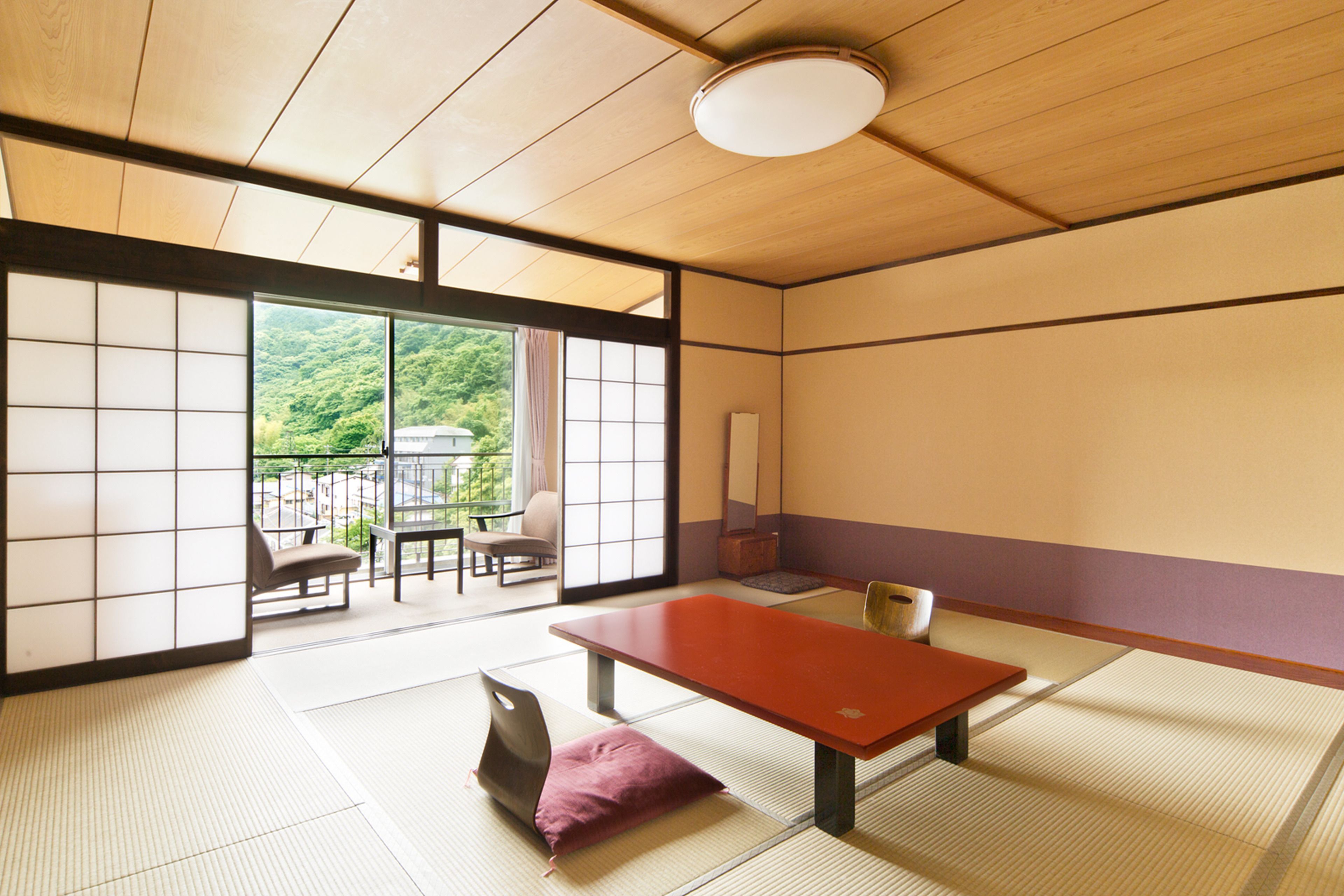 A traditional Japanese room with tatami flooring, a low table, and sliding doors leading to an outdoor area with a view of greenery.
