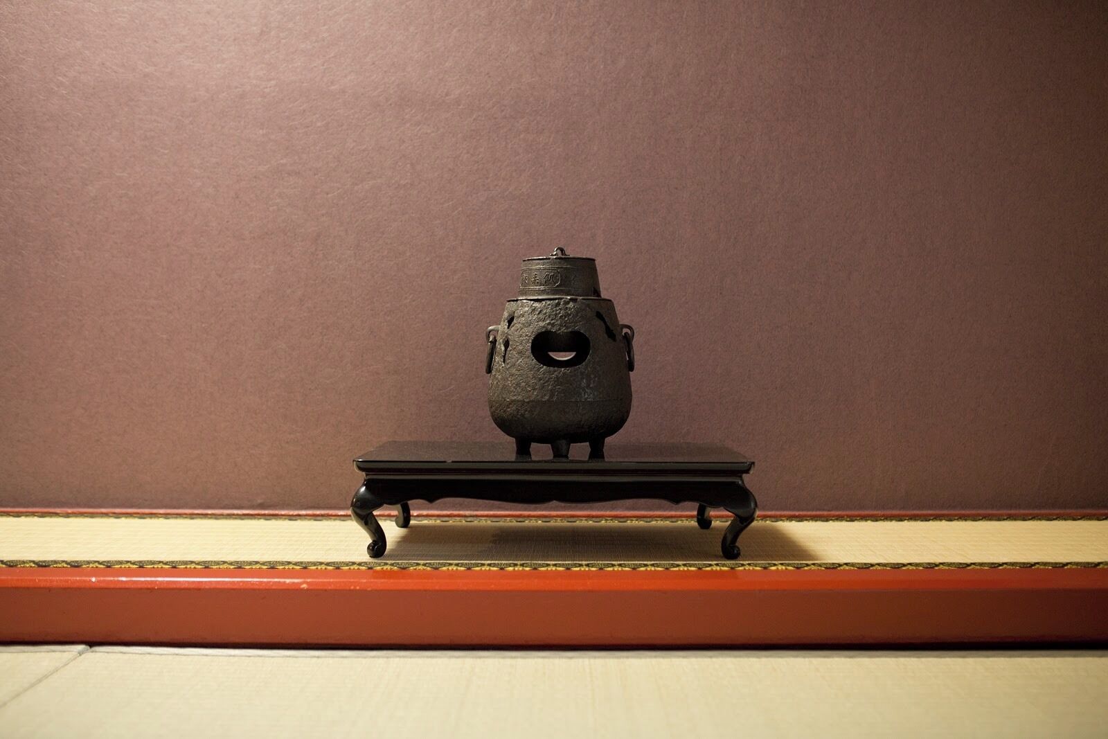 Una pequeña olla de metal decorada sobre una mesa negra frente a una pared lisa.