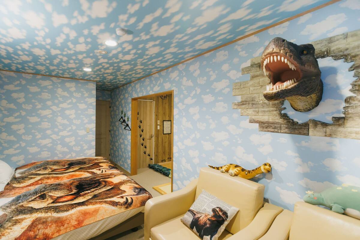 A room with a bed, a chair, a dinosaur head decoration, and a wall with a cloud pattern.