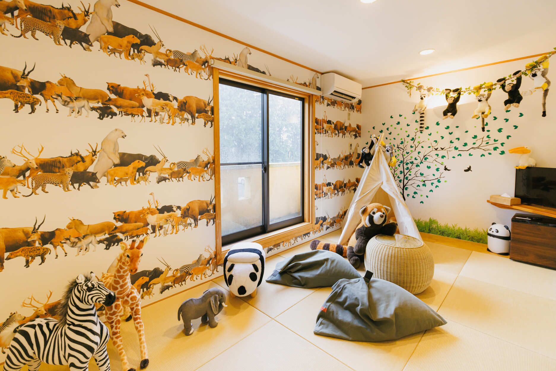 A child's playroom with a large window, stuffed animals, and a wall mural of various animals.