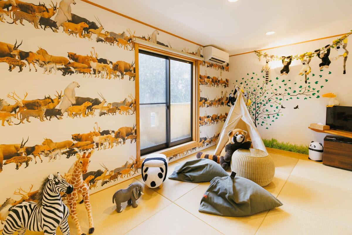 A child's playroom with a large window, stuffed animals, and a wall mural of various animals.