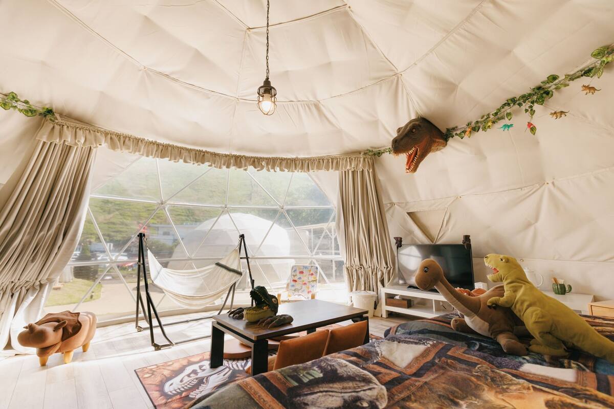 A cozy tented room with a hammock, a table, a TV, and dinosaur toys.
