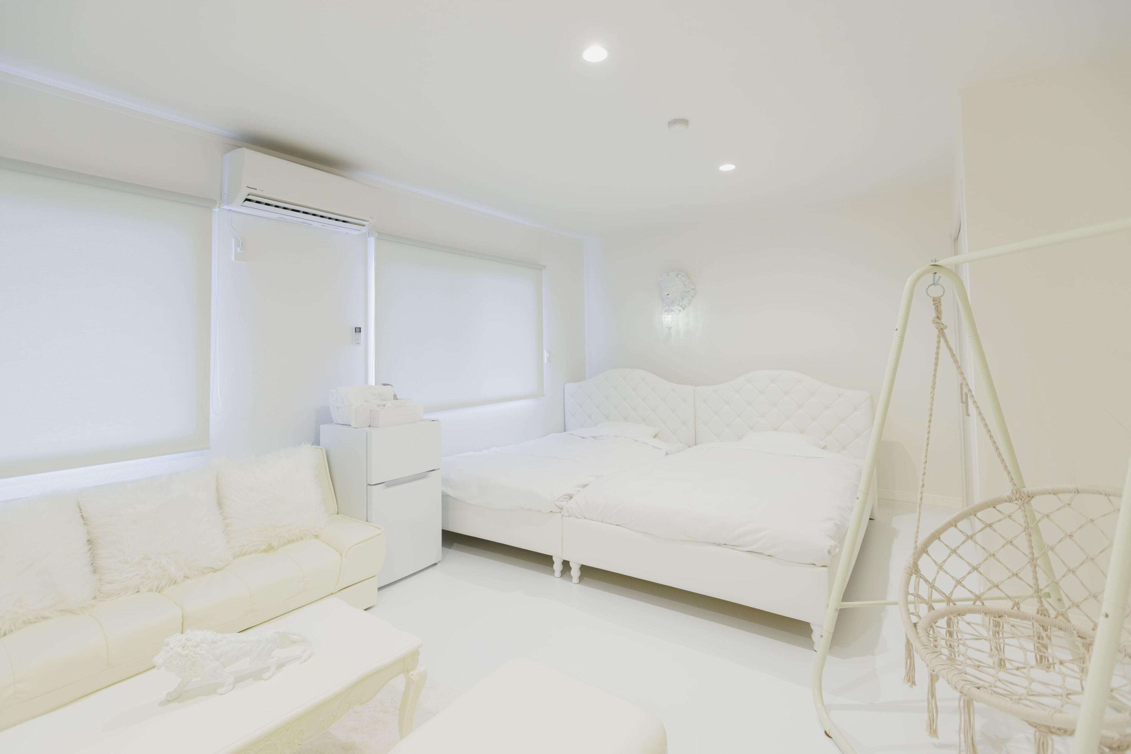 A white room with a bed, a sofa, a hanging chair, and a window.