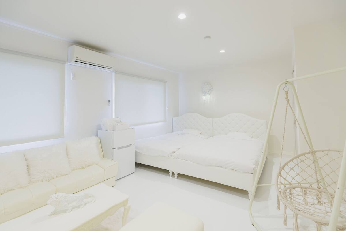 A white room with a bed, a sofa, a hanging chair, and a window.
