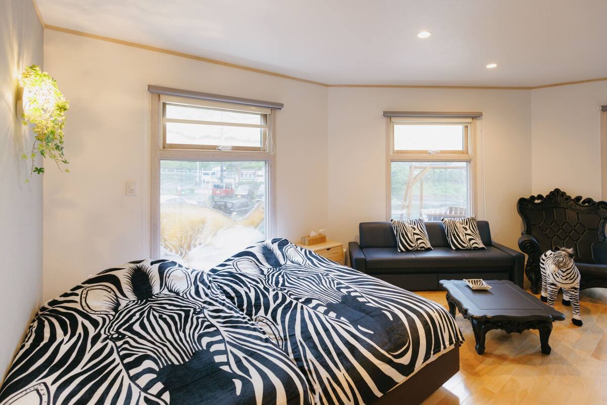 A room with a zebra-patterned bed, a dark sofa, a wooden coffee table, and a zebra-patterned rug.