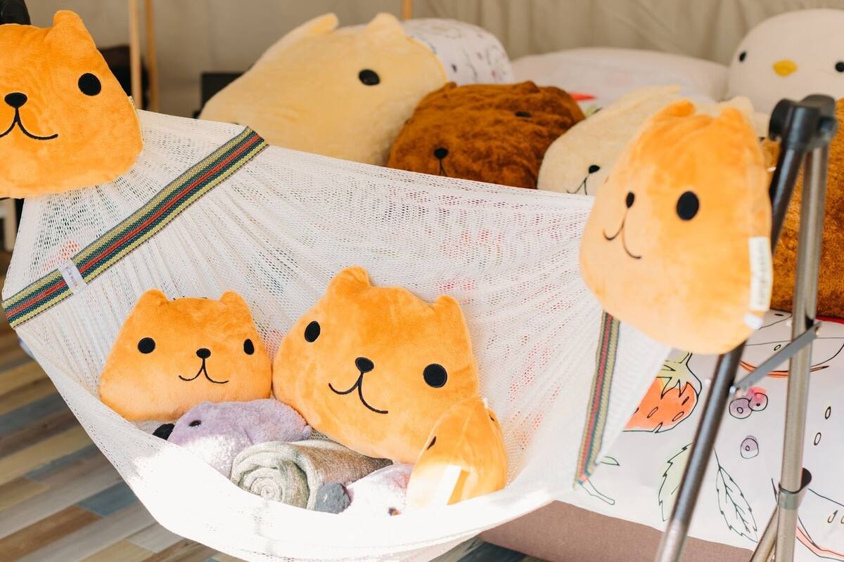 A hammock with plush bear-shaped pillows, a striped fabric, and a metal frame.