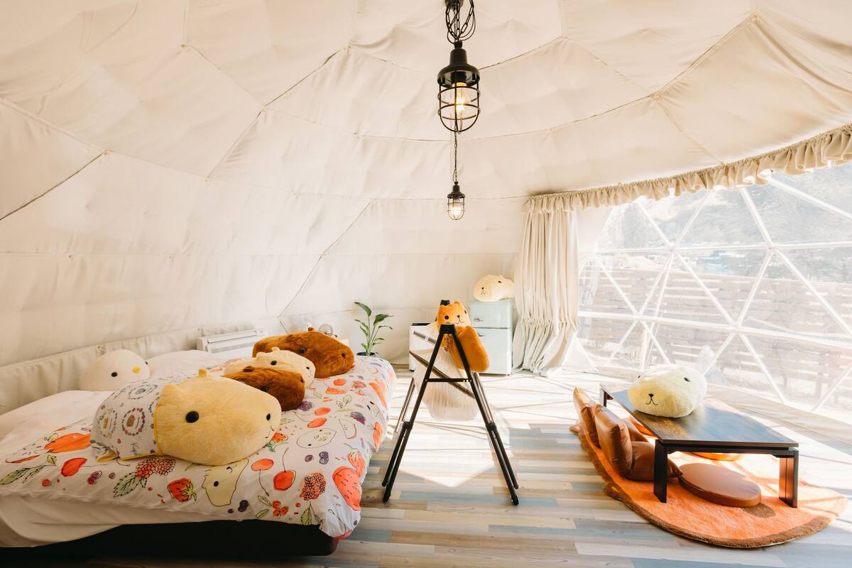 A cozy tent-style room with a bed, pillows, a small table, and a window with a view.