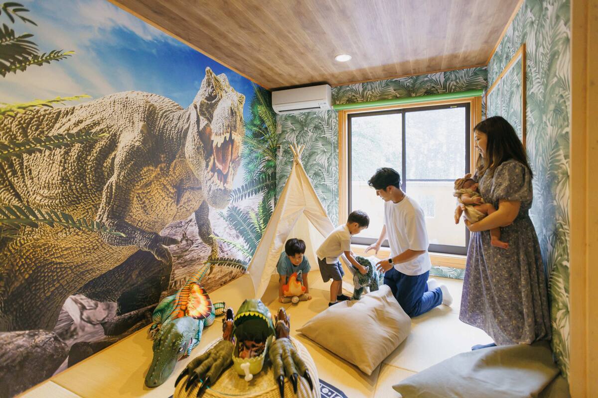 A room with a mural of dinosaurs, a tent, and a large window.