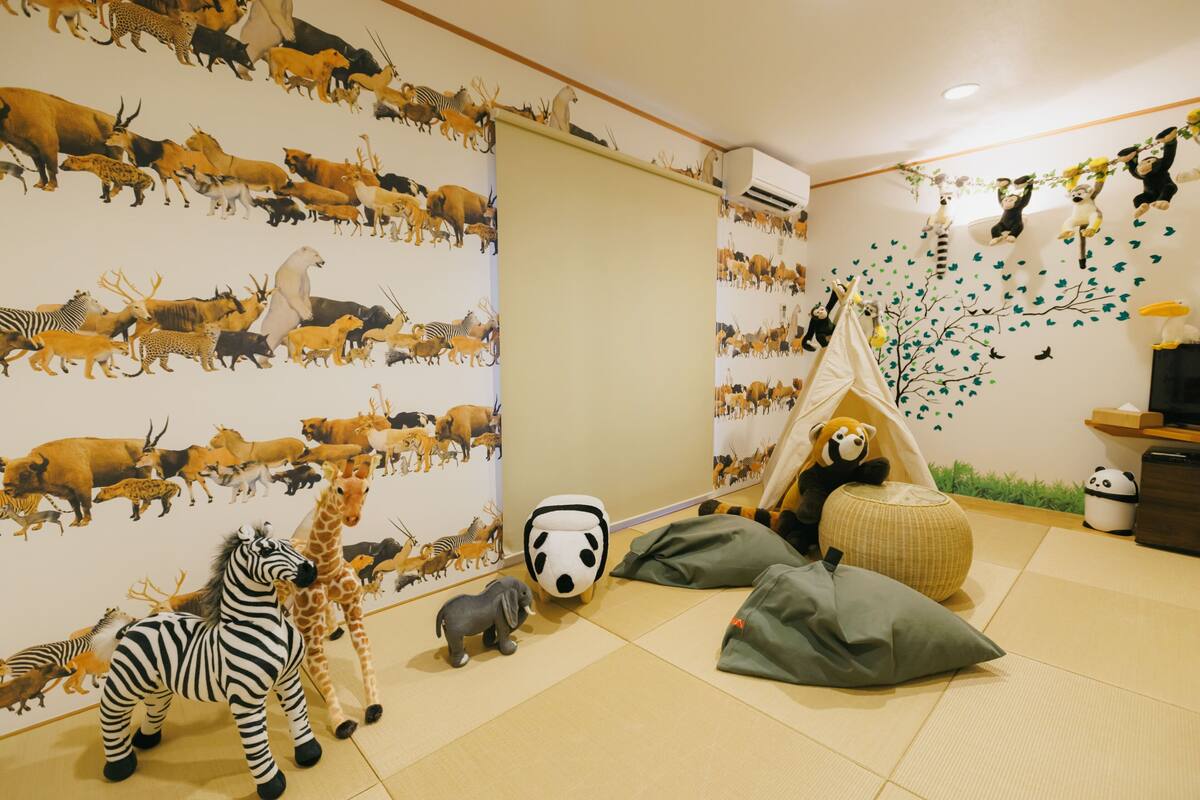A room with a wall mural of various animals, a play tent, and a panda plush toy.