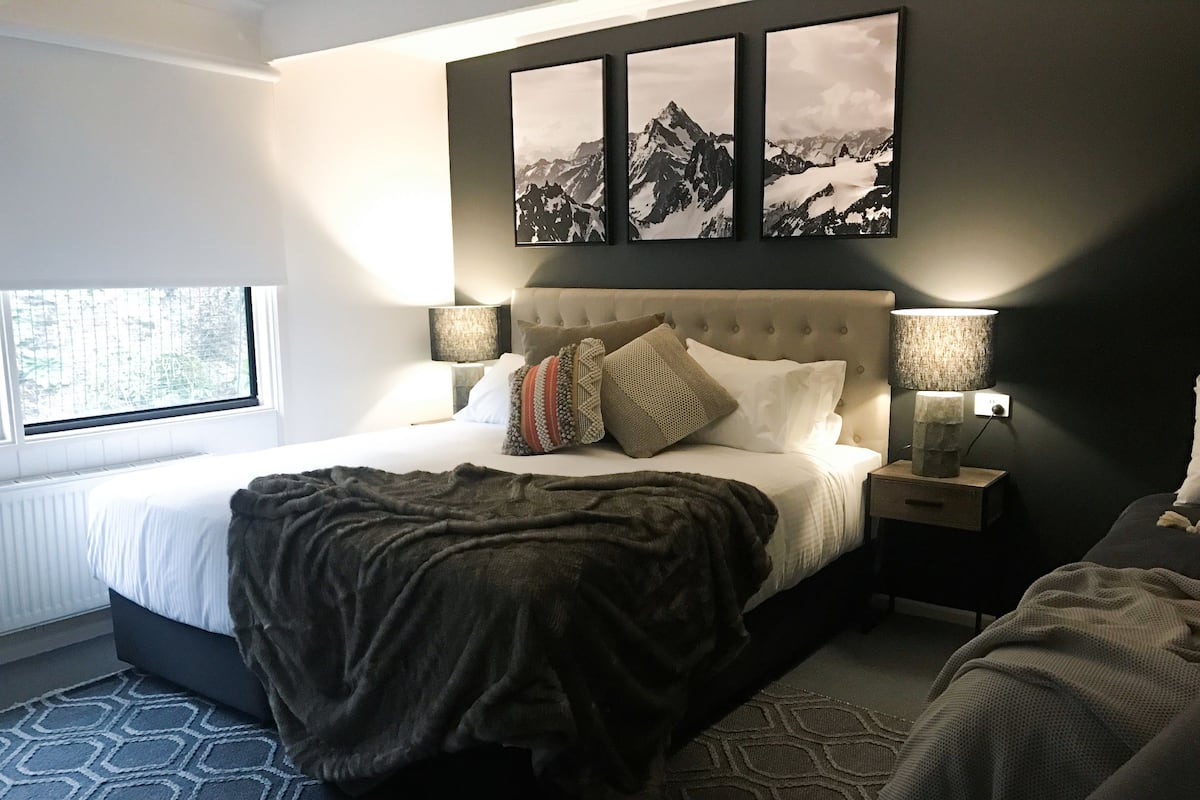 Une chambre à coucher avec un grand lit, une fenêtre, un tableau accroché au mur et une table de chevet avec une lampe.