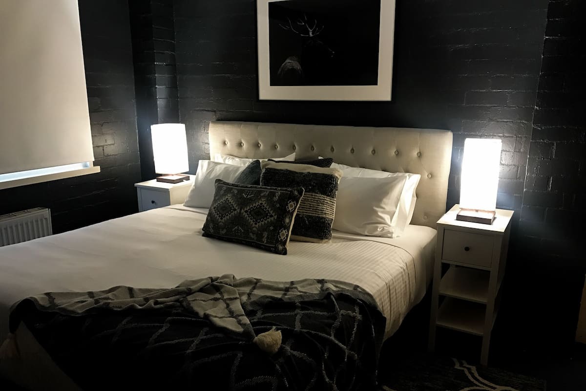 Un lit bien fait, agrémenté d’un couvre-lit à motifs, d’une tête de lit capitonnée et de deux lampes de chevet.