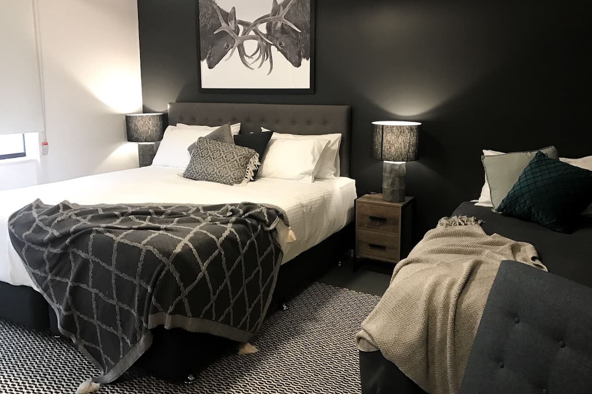 Une chambre à coucher moderne avec un grand lit, des tables de chevet, une œuvre d’art accrochée au mur et un tapis à motifs.