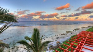 A beach with a red wooden walkway, palm trees, and a view of the ocean. - Kiikii Inn & Suites (Rarotonga)