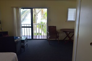 A room with a bed, a desk, a chair, a table, and a balcony with a view of palm trees. - Kiikii Inn & Suites (Rarotonga)