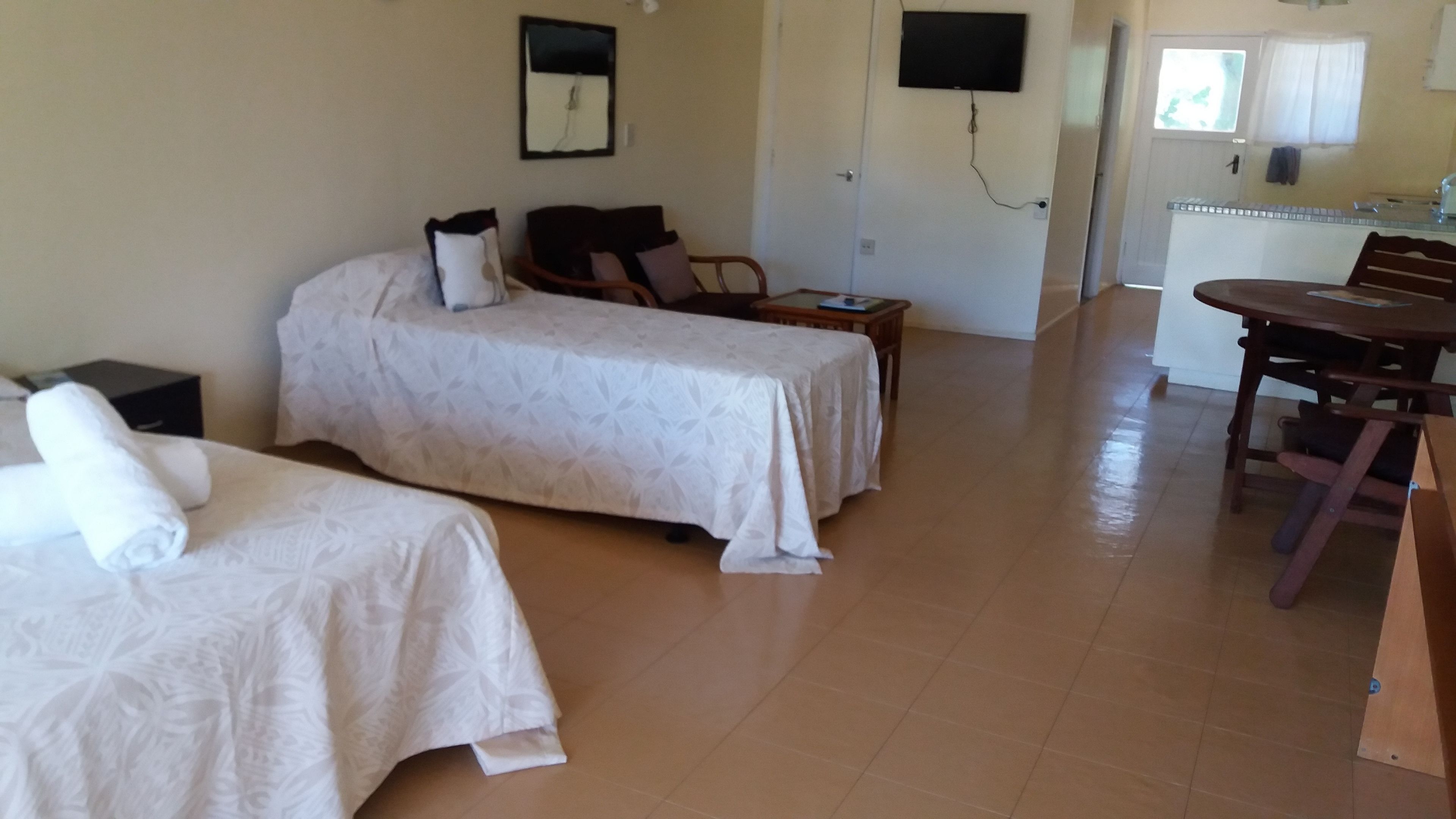 Habitación de hotel con dos camas, una mesita, una silla y una zona de kitchenette.