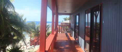 A wooden balcony with a view of the beach and ocean.