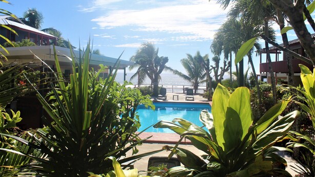 A pool surrounded by tropical plants and palm trees, with a clear sky above. - Kiikii Inn & Suites (Rarotonga)