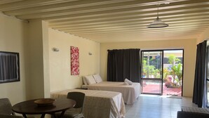 A room with two beds, a dining table with chairs, a ceiling fan, and a view of the outside garden. - Kiikii Inn & Suites (Rarotonga)