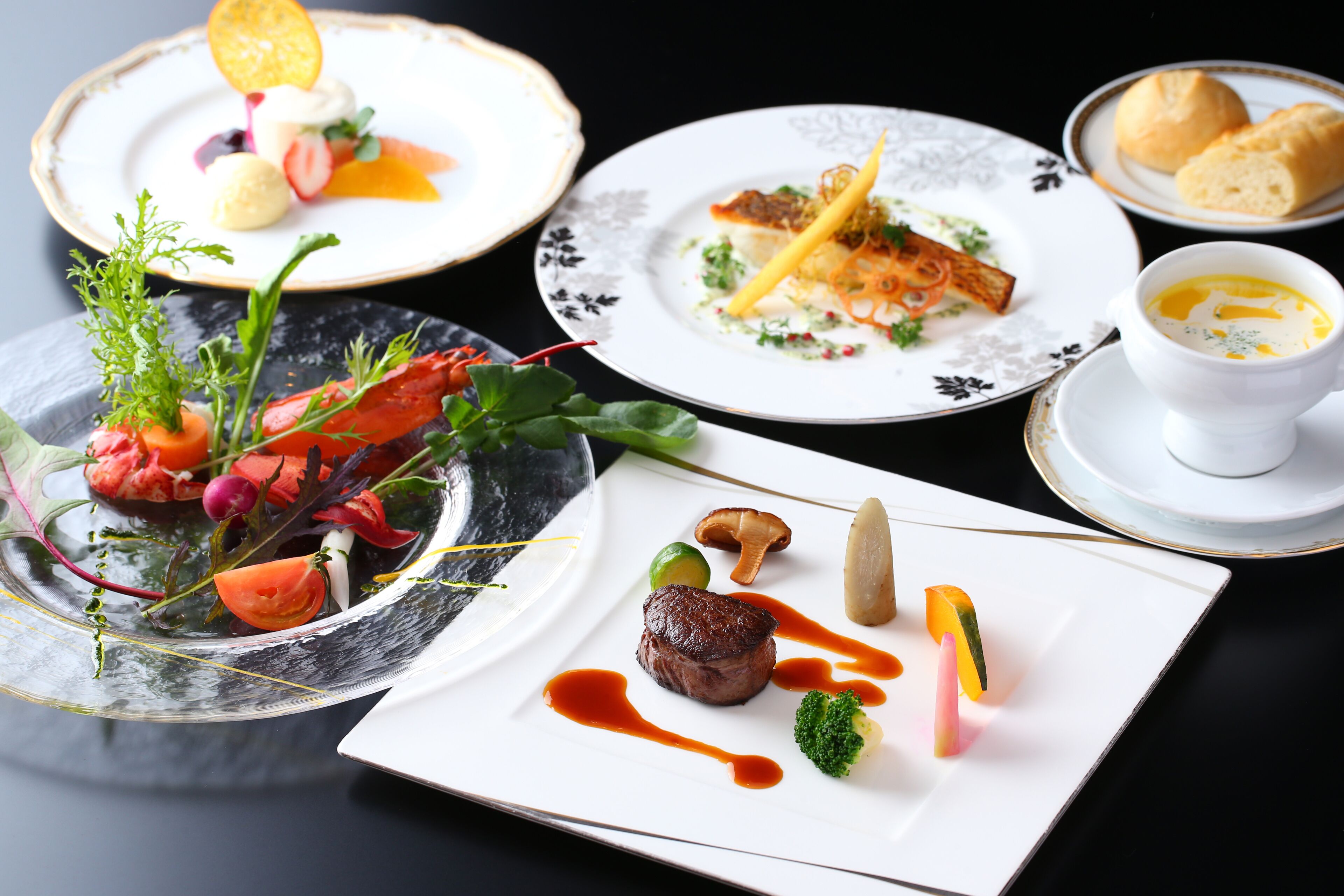 A variety of dishes on plates, including a lobster, steak, and vegetables.