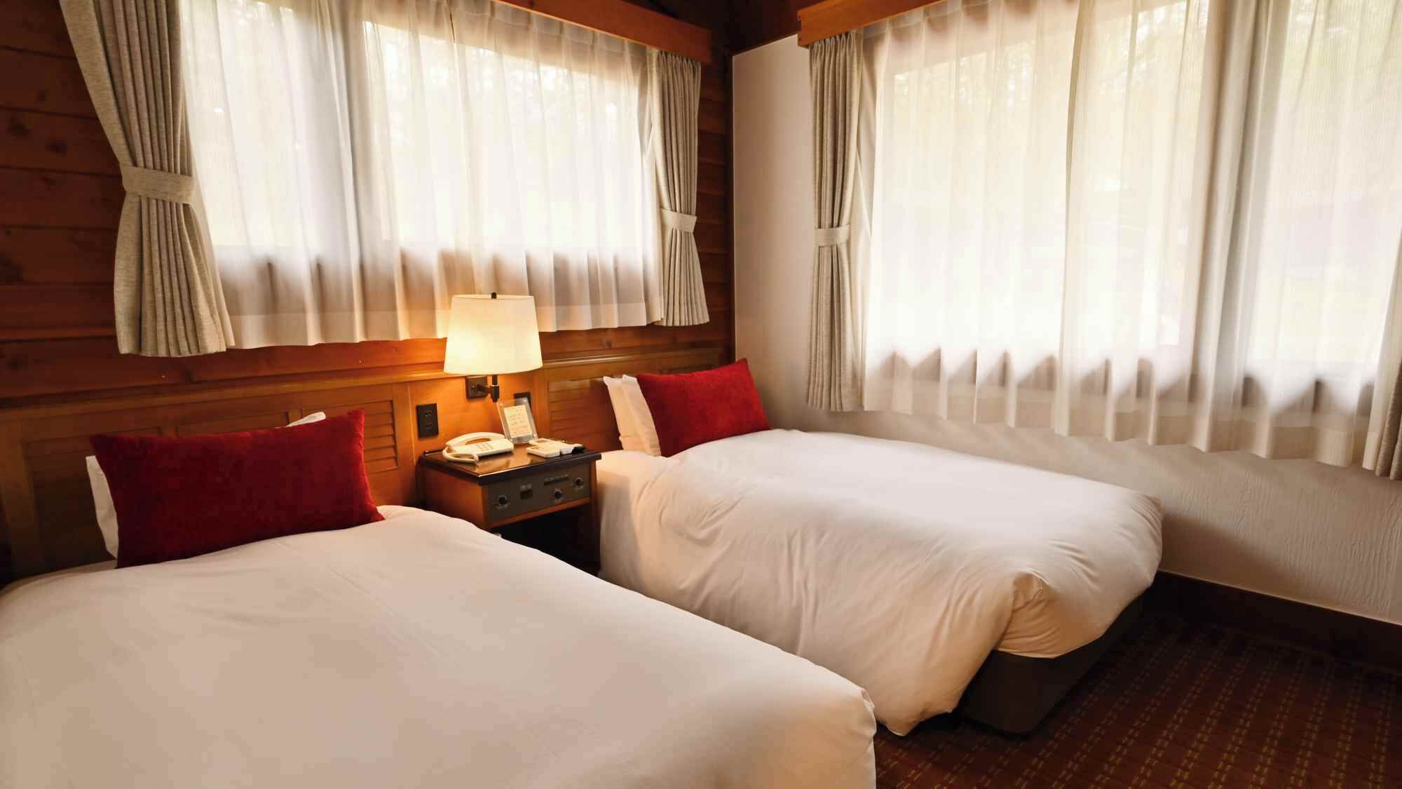 Une chambre d’hôtel avec deux lits, une table de chevet avec une lampe et des rideaux aux fenêtres.