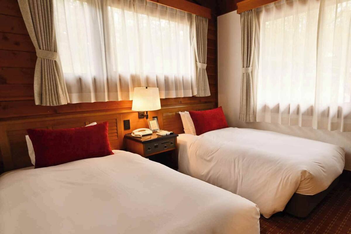 Una habitación de hotel con dos camas, una mesita de noche con lámpara y cortinas en las ventanas.