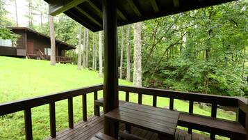 A wooden deck with a picnic table and benches, overlooking a grassy area with a cabin.