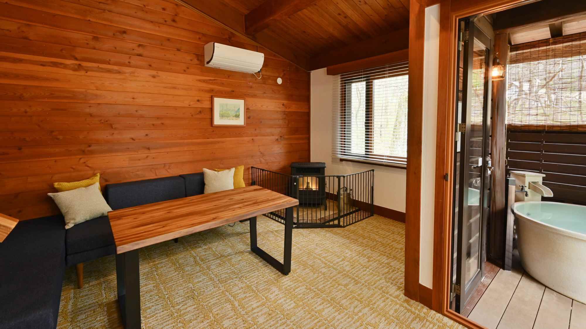 A wooden cabin interior with a sofa, a table, a fireplace, and a bathroom with a sink and toilet.
