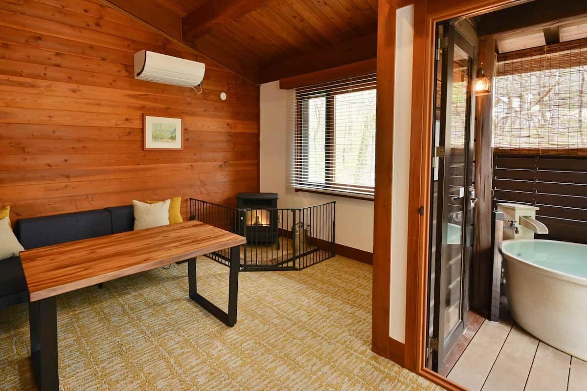 A wooden cabin interior with a sofa, a table, a fireplace, and a bathroom with a sink and toilet.