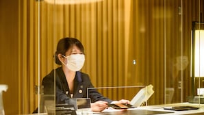 A reception desk with a woman seated behind it, a nameplate, and a glass partition. - Tateshina Tokyu Hotel (Chino)