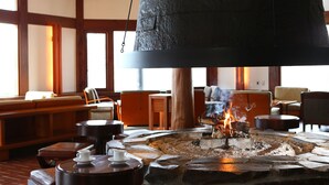 A stone fire pit with a hanging bell above it, surrounded by wooden furniture and a large window. - Tateshina Tokyu Hotel (Chino)