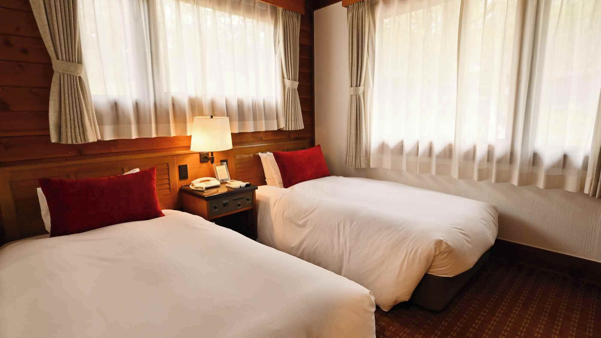 Une chambre d’hôtel avec deux lits, une table de chevet avec une lampe et des rideaux aux fenêtres.