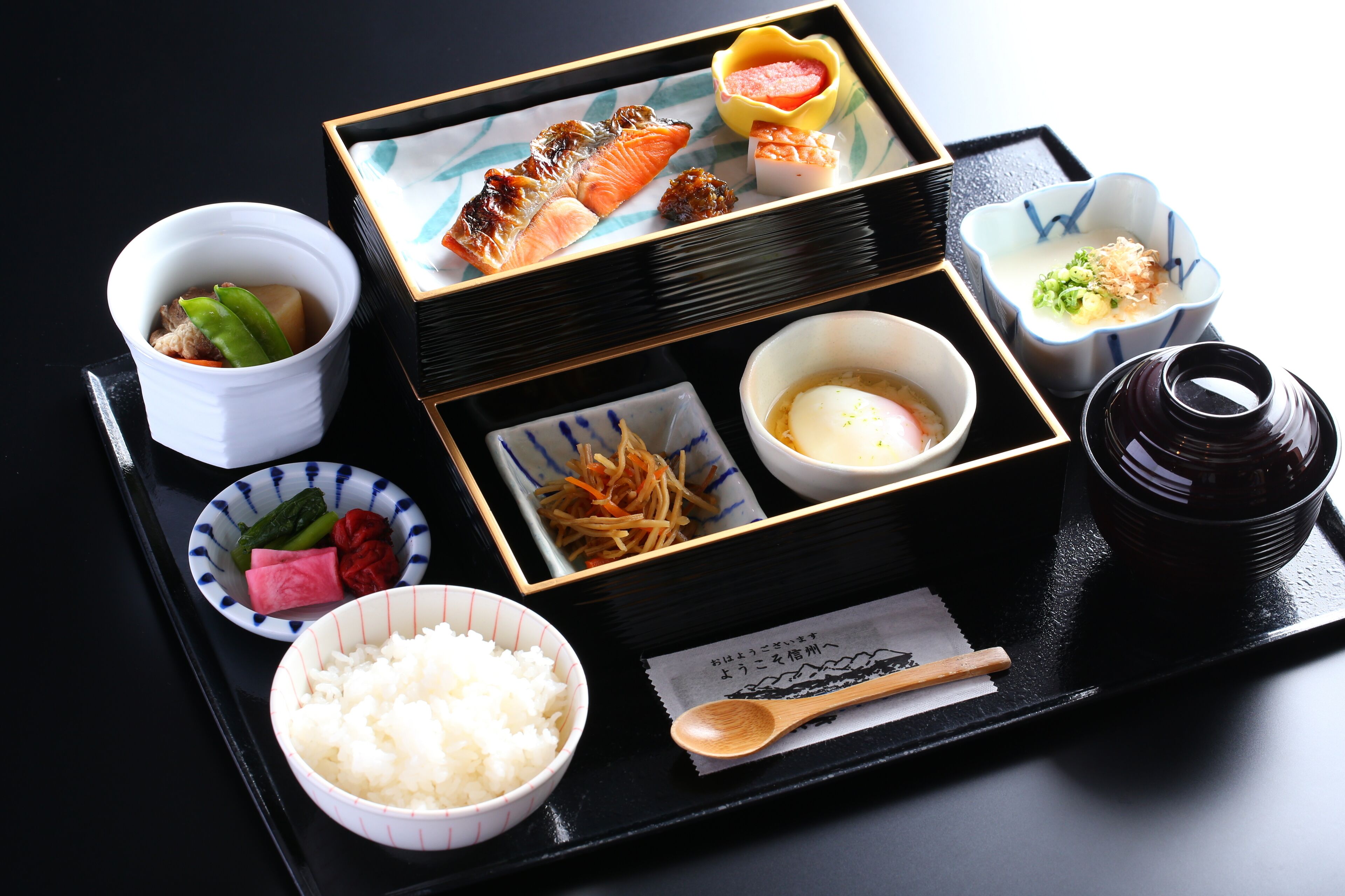 A traditional Japanese meal with various dishes including rice, fish, and pickles, served on a black tray.
