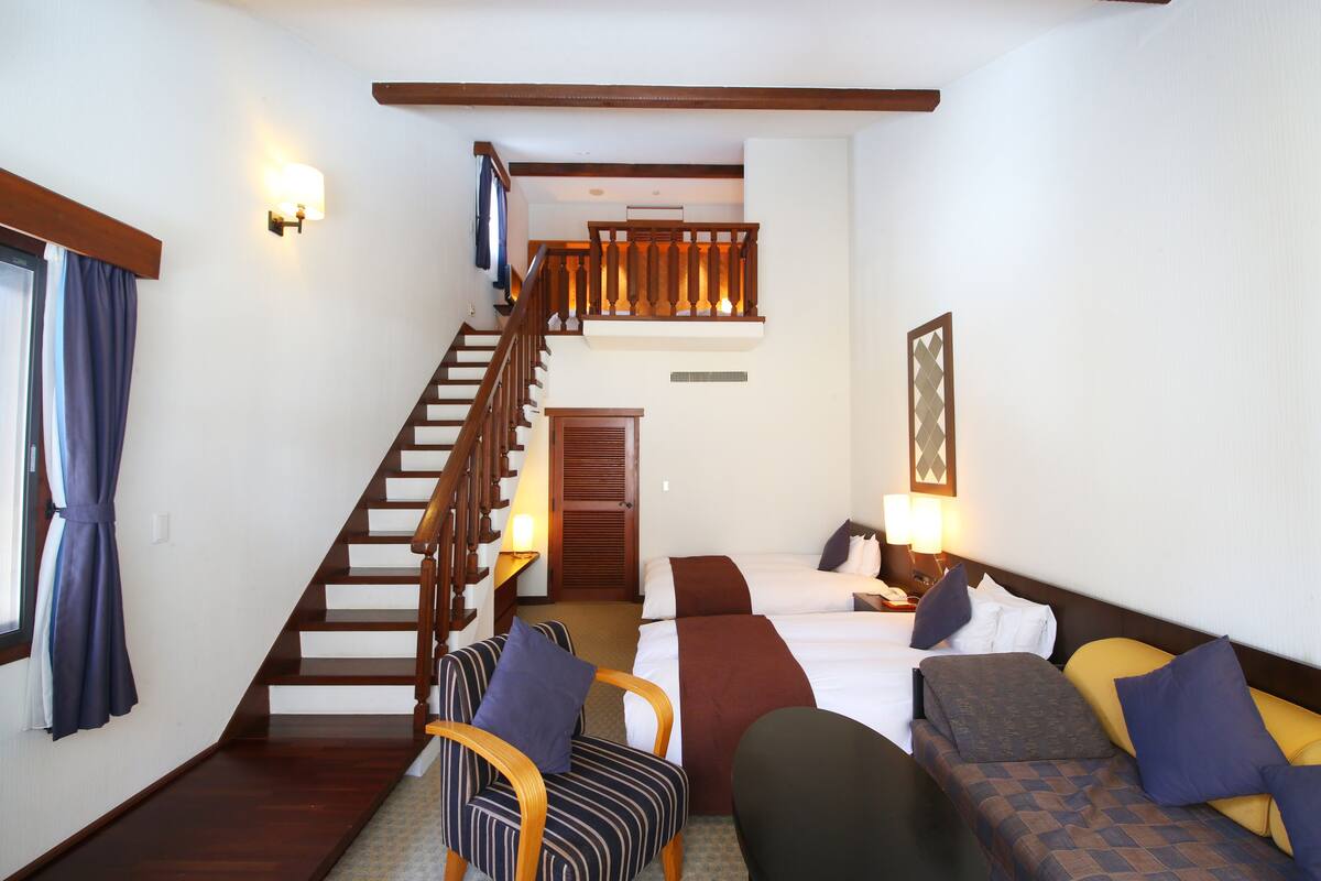 Habitación de hotel con escalera de madera, dos camas, un sofá y una silla.