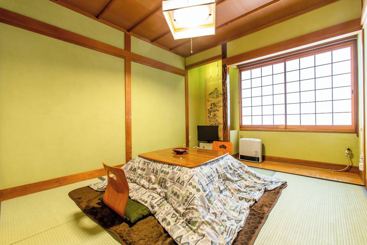 A traditional Japanese room with tatami flooring, a low table, a cushion, and a sliding door.