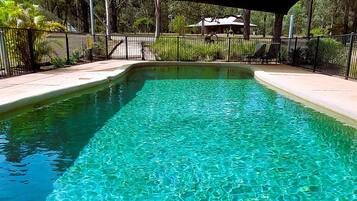 A rectangular pool with clear water, surrounded by a black metal fence and a paved walkway.